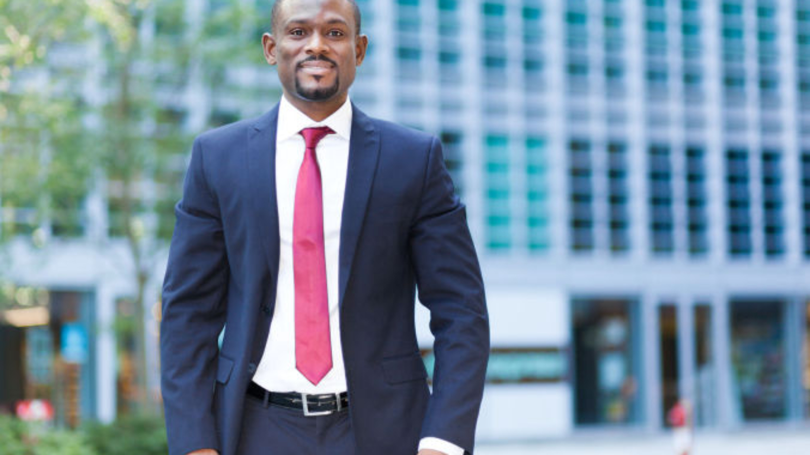 Confident businessman in a suit with a red tie standing outside a modern office building in the city