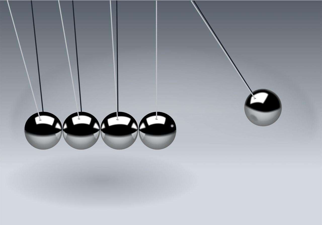 Newton's cradle with five metallic balls in motion, demonstrating principles of physics and momentum.