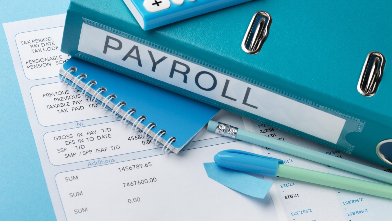 Close-up of payroll documents, a blue binder labeled 'PAYROLL', a calculator, a notebook, and various office supplies like pens, highlighters, and paper clips, all arranged on a blue background.