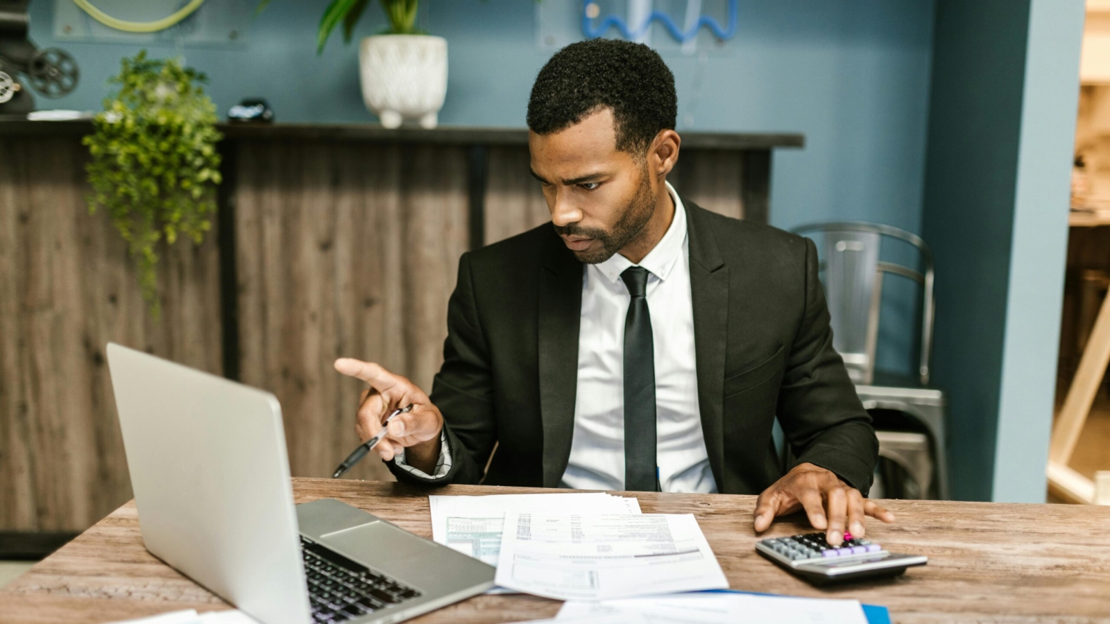 Businessman in a suit working with a laptop, calculator, and financial documents in an office setting.