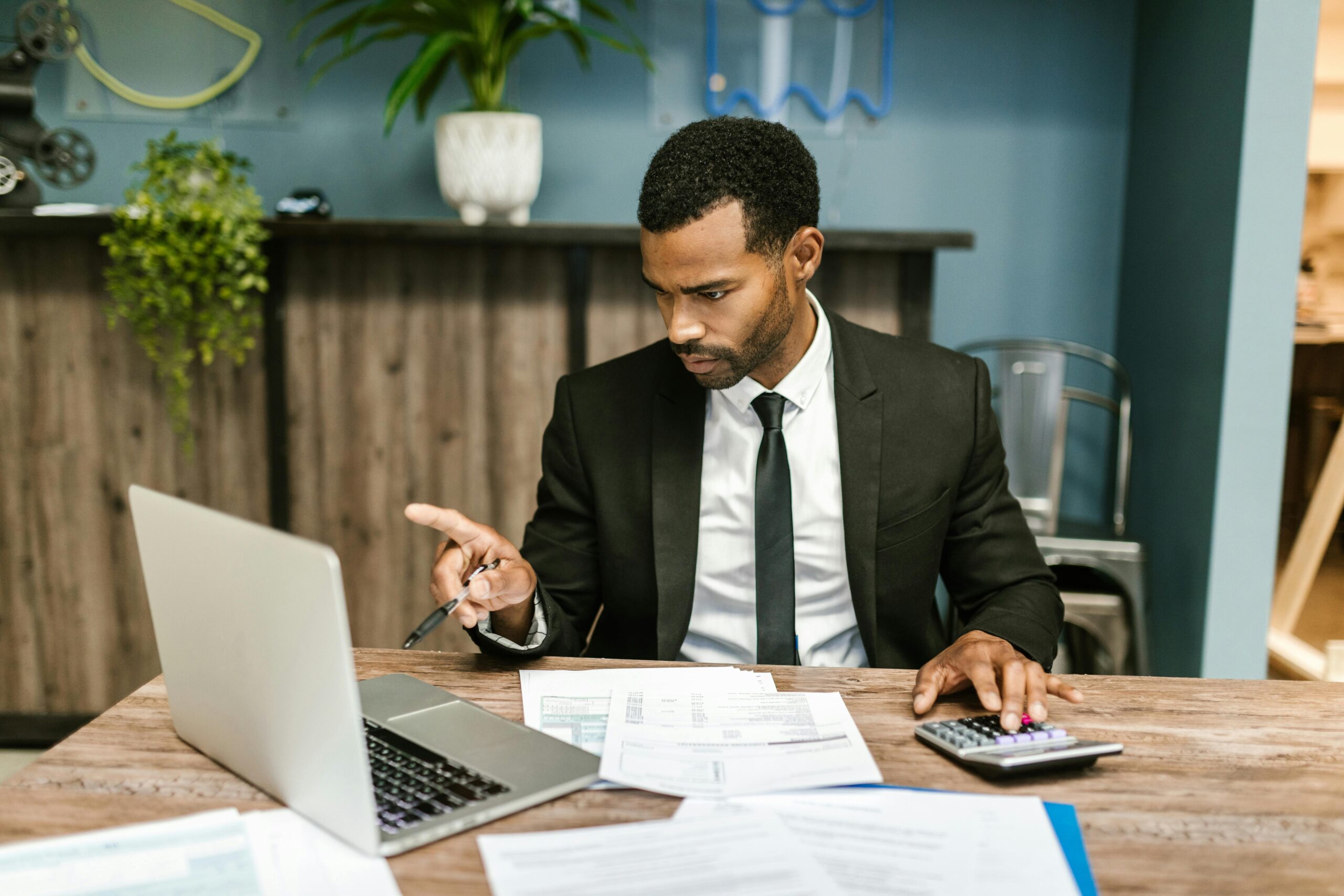Businessman in a suit working with a laptop, calculator, and financial documents in an office setting.